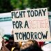 Crowd holding a protest sign with 'Fight Today for a Better Tomorrow', outdoors and during the day.